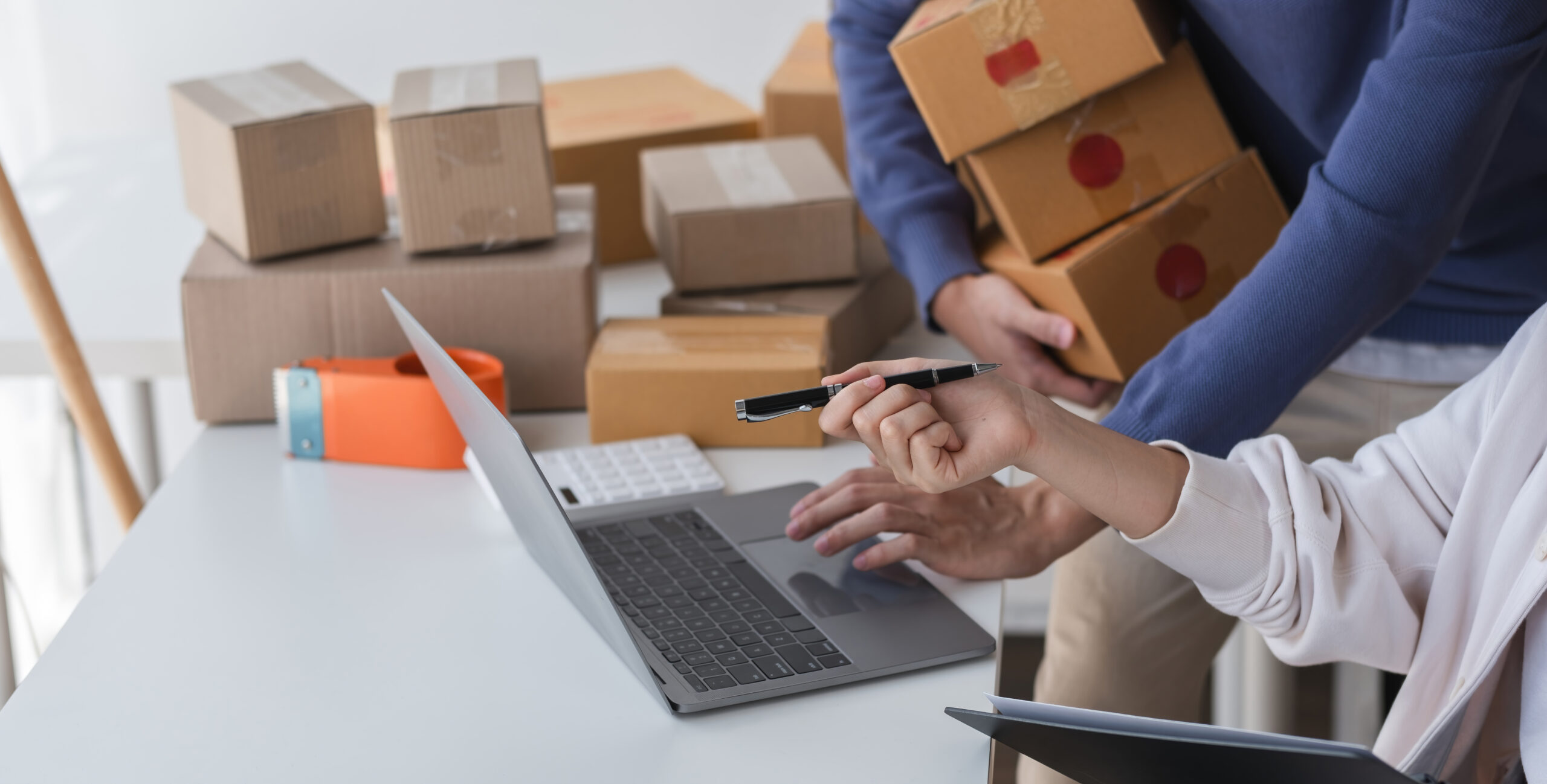 A happy Asian online shopping entrepreneur couple takes orders and packs products to send to customers together in their office.